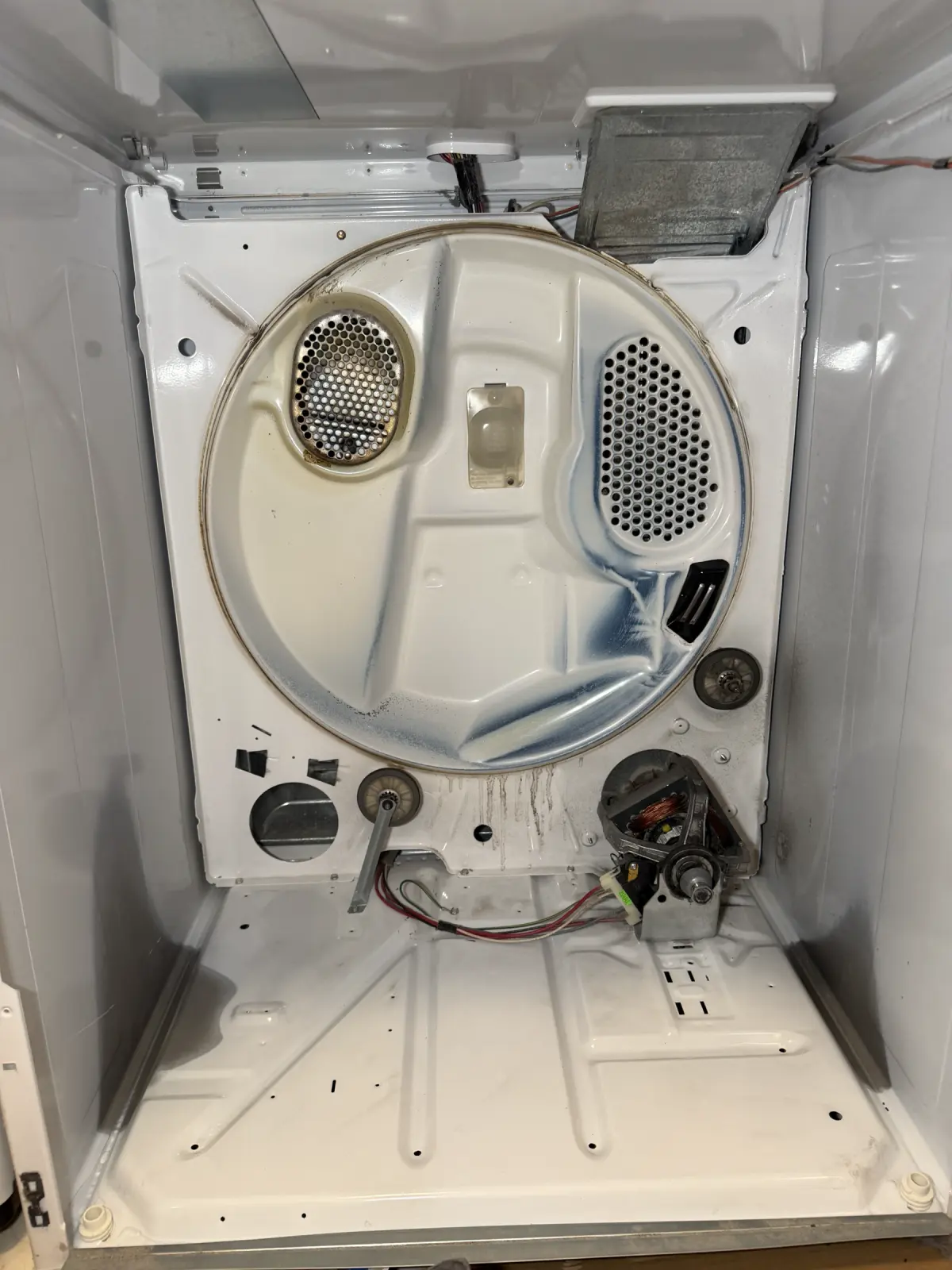 Inside a disassembled dryer showing the motor, support rollers, wiring, and rear bulkhead