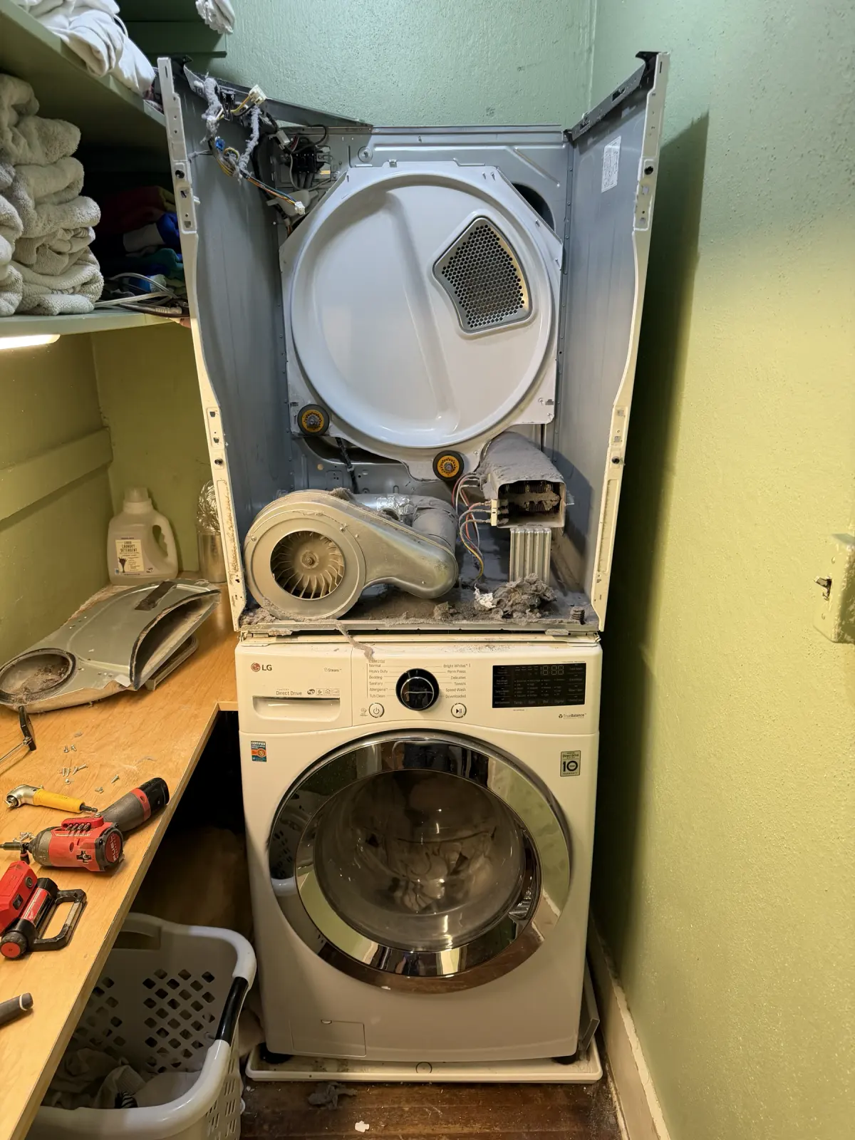 Stacked LG dryer opened for service showing lint around the blower housing and airflow path
