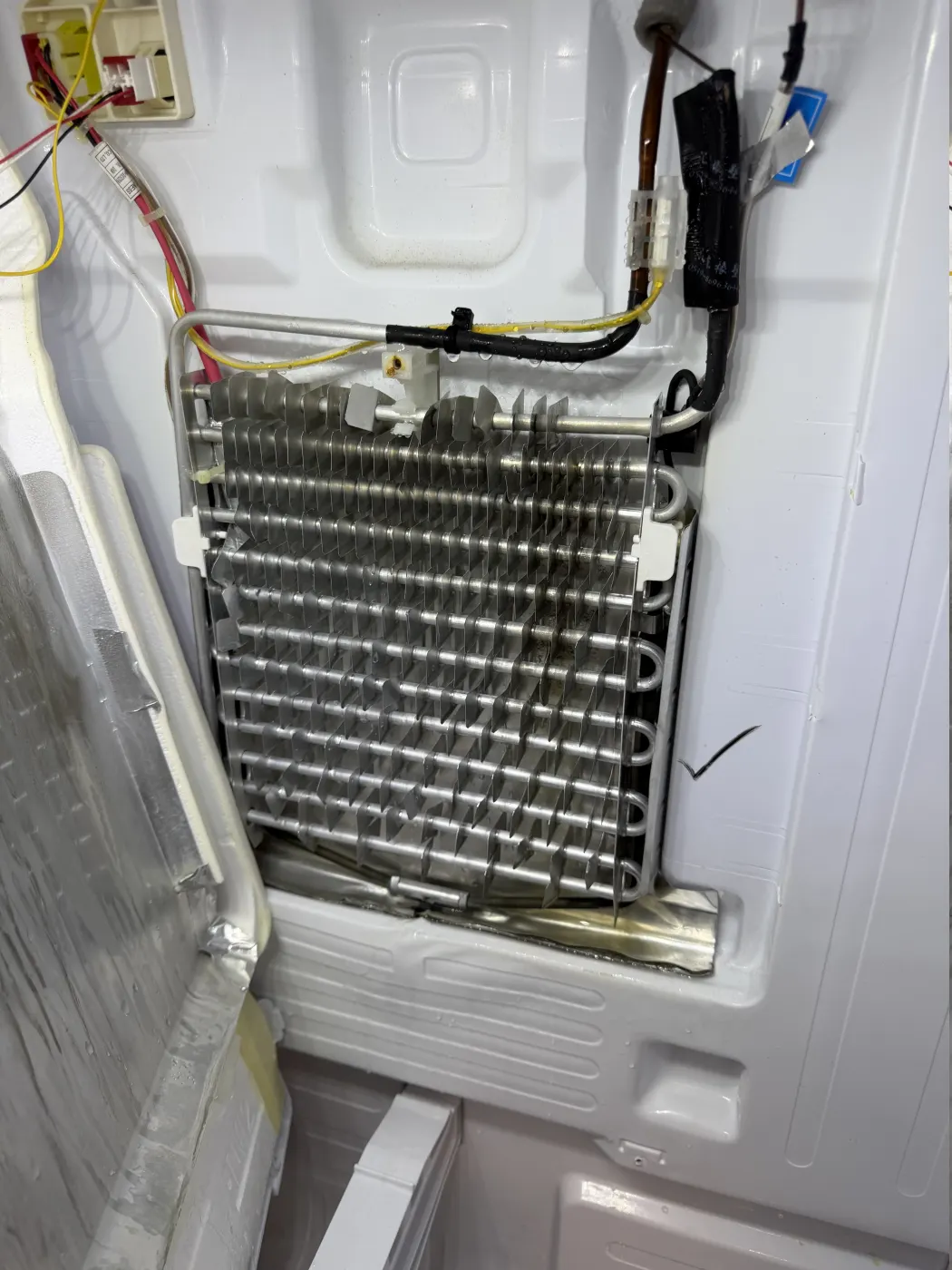 Refrigerator evaporator coil and refrigerant tubing exposed during professional service