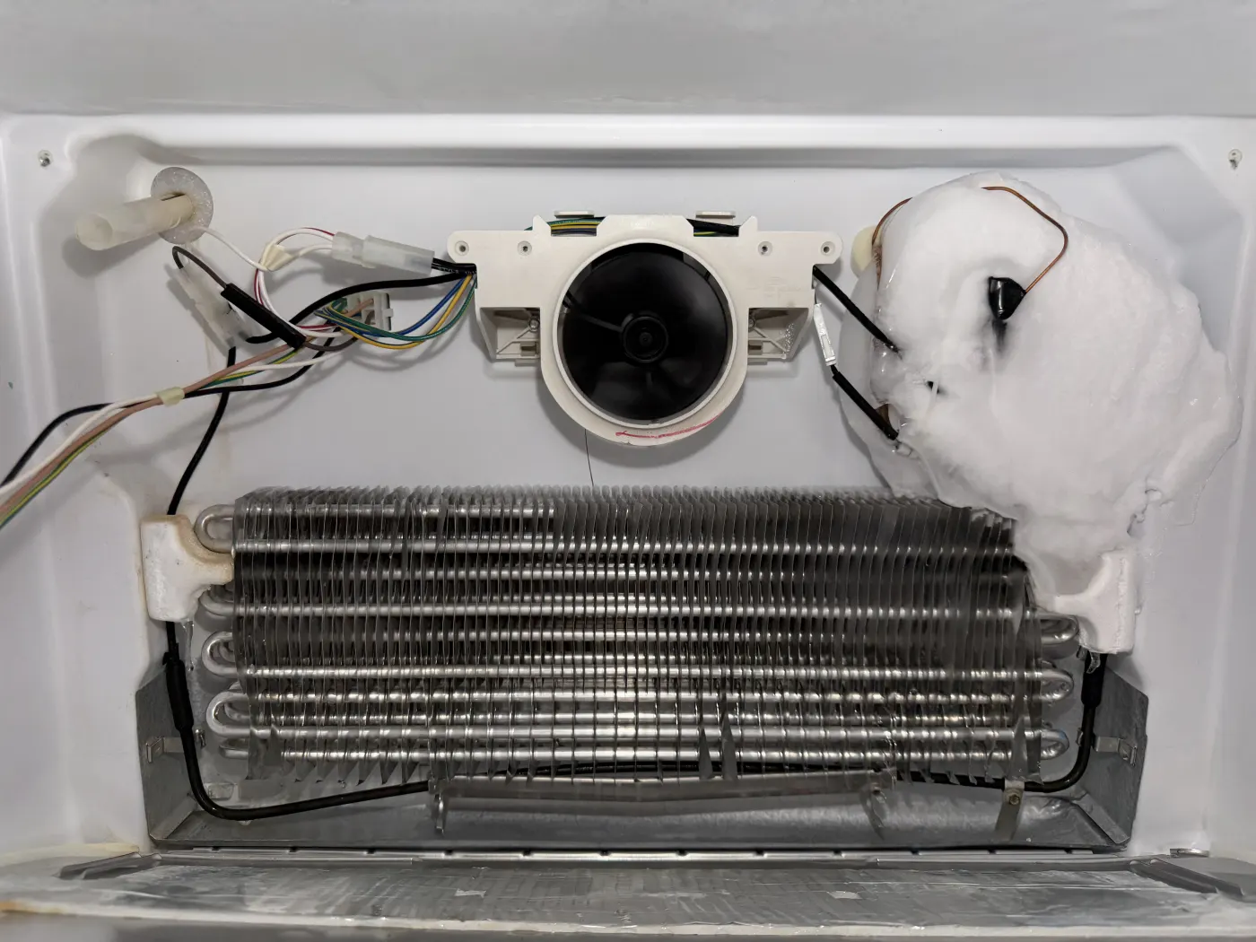 Refrigerator evaporator fan beside ice buildup with the interior panel removed
